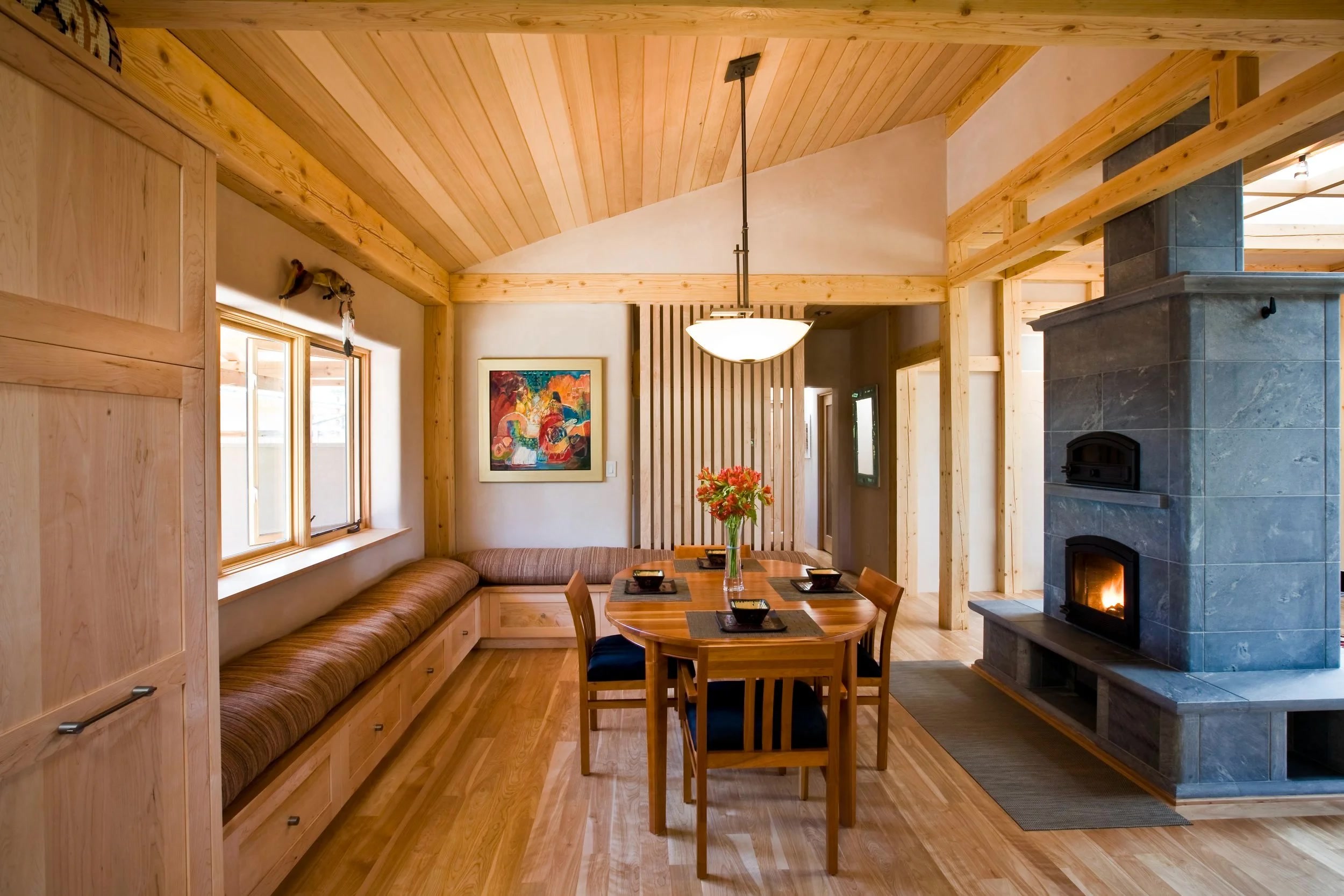 Light-filled timber-frame dining room with banquette seating and soapstone masonry heater