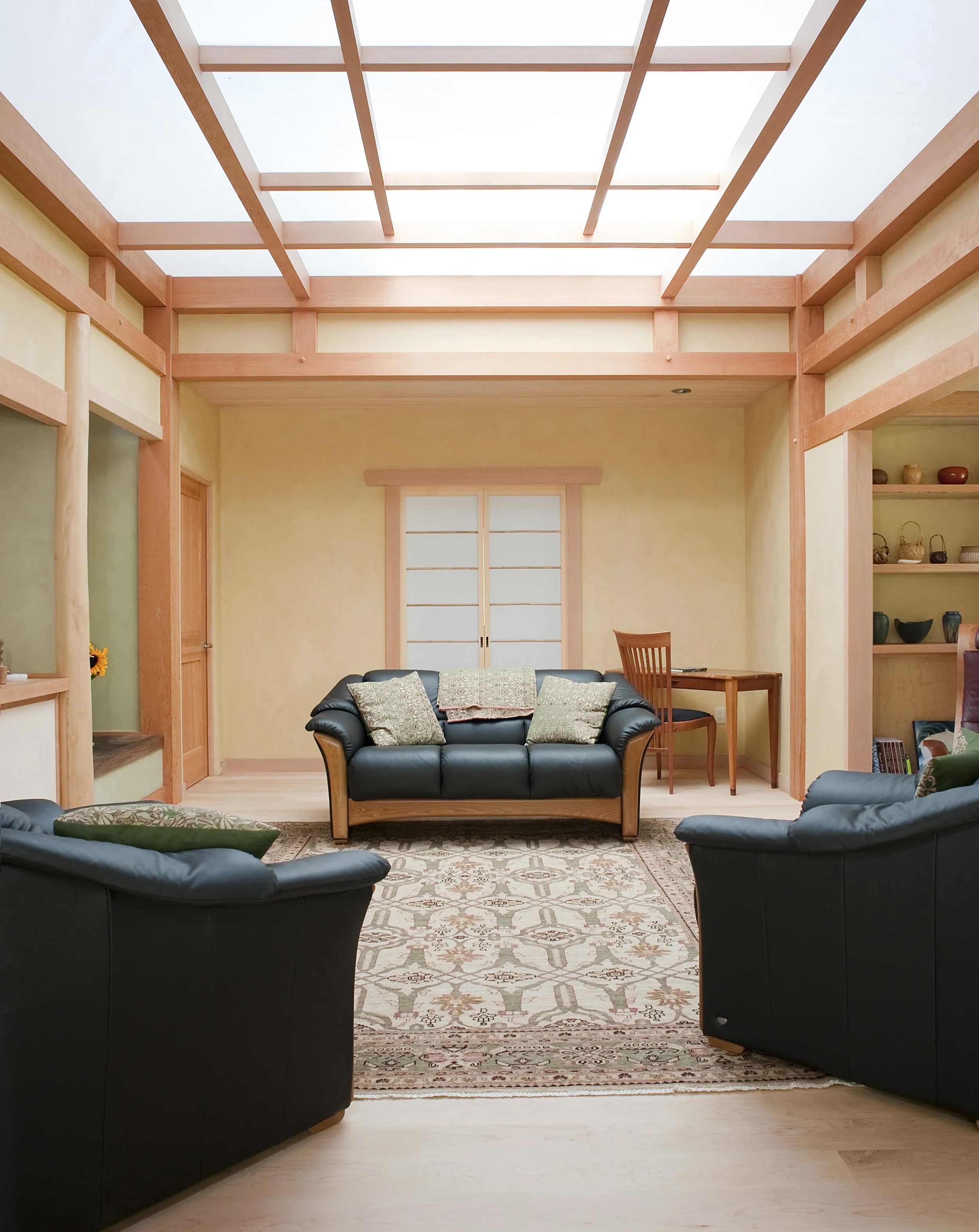 Light-filled sitting area with timber frame, shoji-style doors, natural plaster walls, and a large skylight grid above