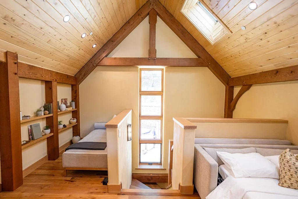 Vaulted timber-frame loft sleeping area with skylights, built-in shelving, and a daybed under the gable