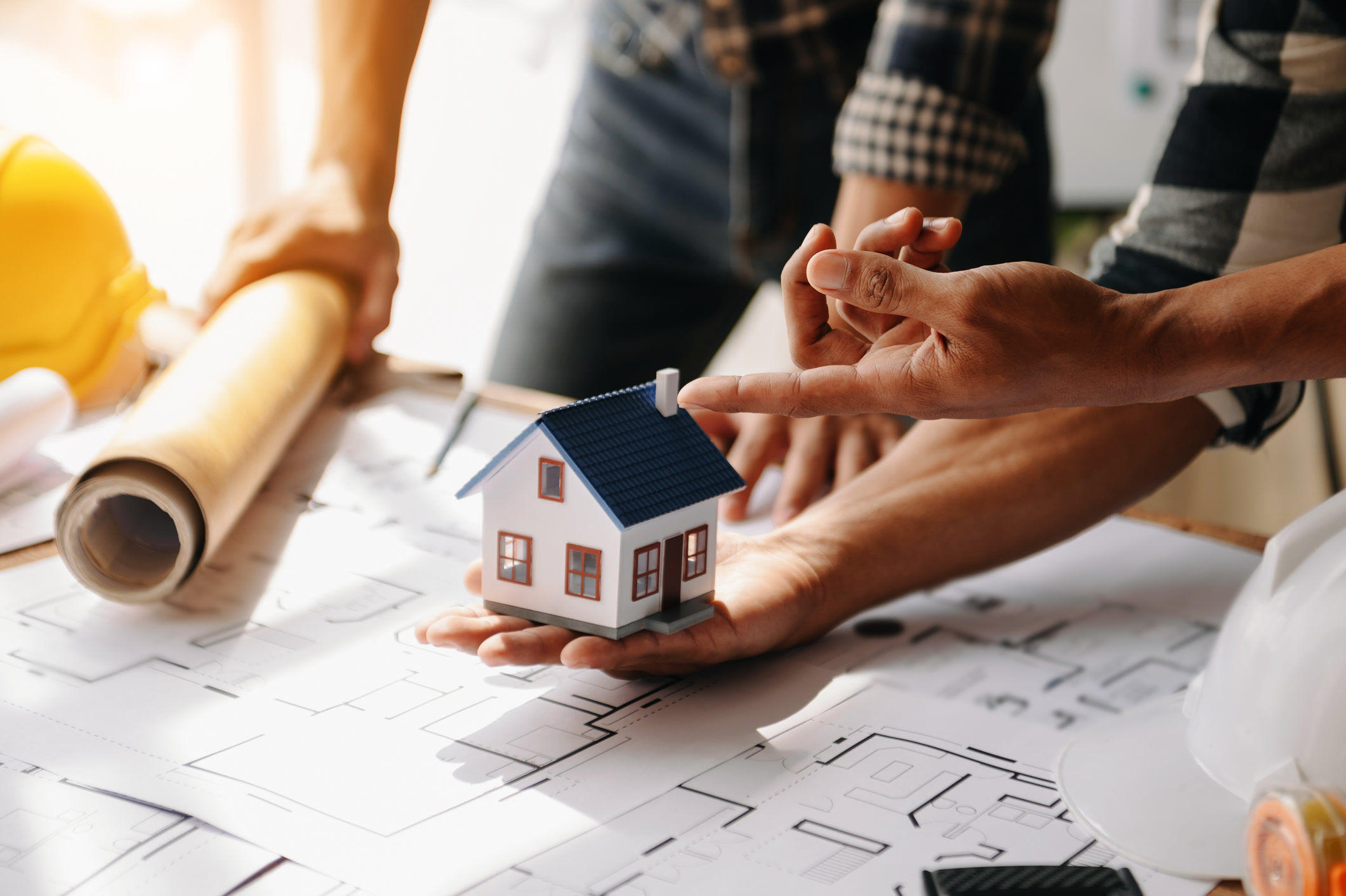 Architects and builders reviewing a miniature house model and blueprints