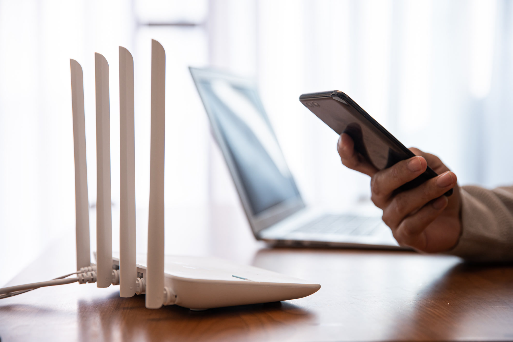 Multi-antenna WiFi router on a desk with smartphone and laptop in soft window light